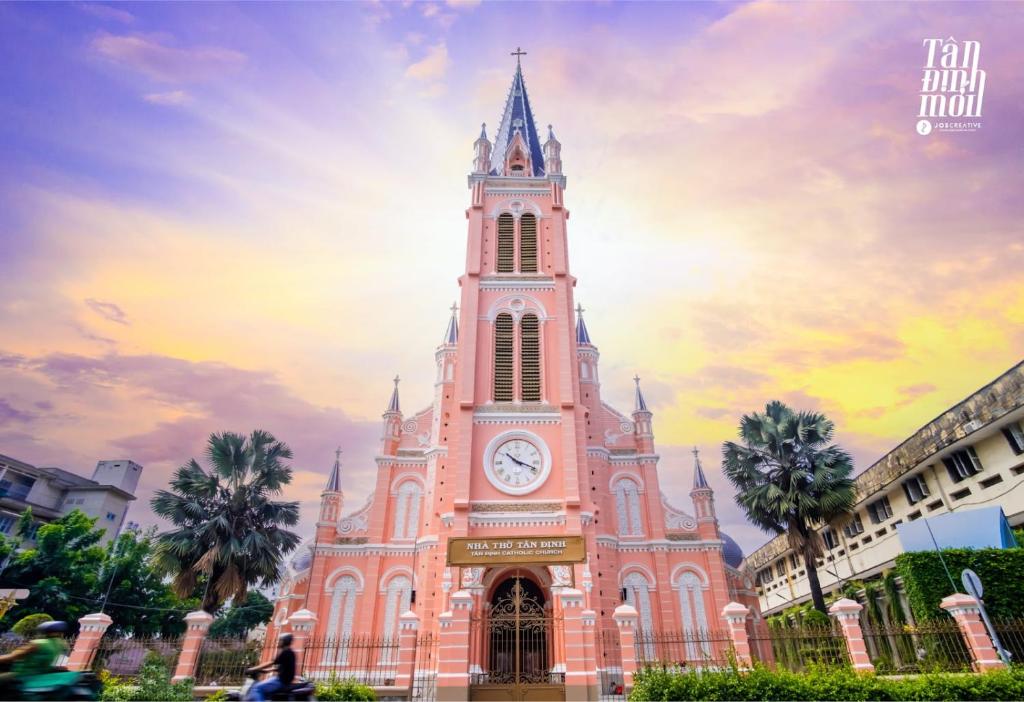 eine Kirche mit einem Uhrturm vor einem Sonnenuntergang in der Unterkunft Jomo in Ho-Chi-Minh-Stadt