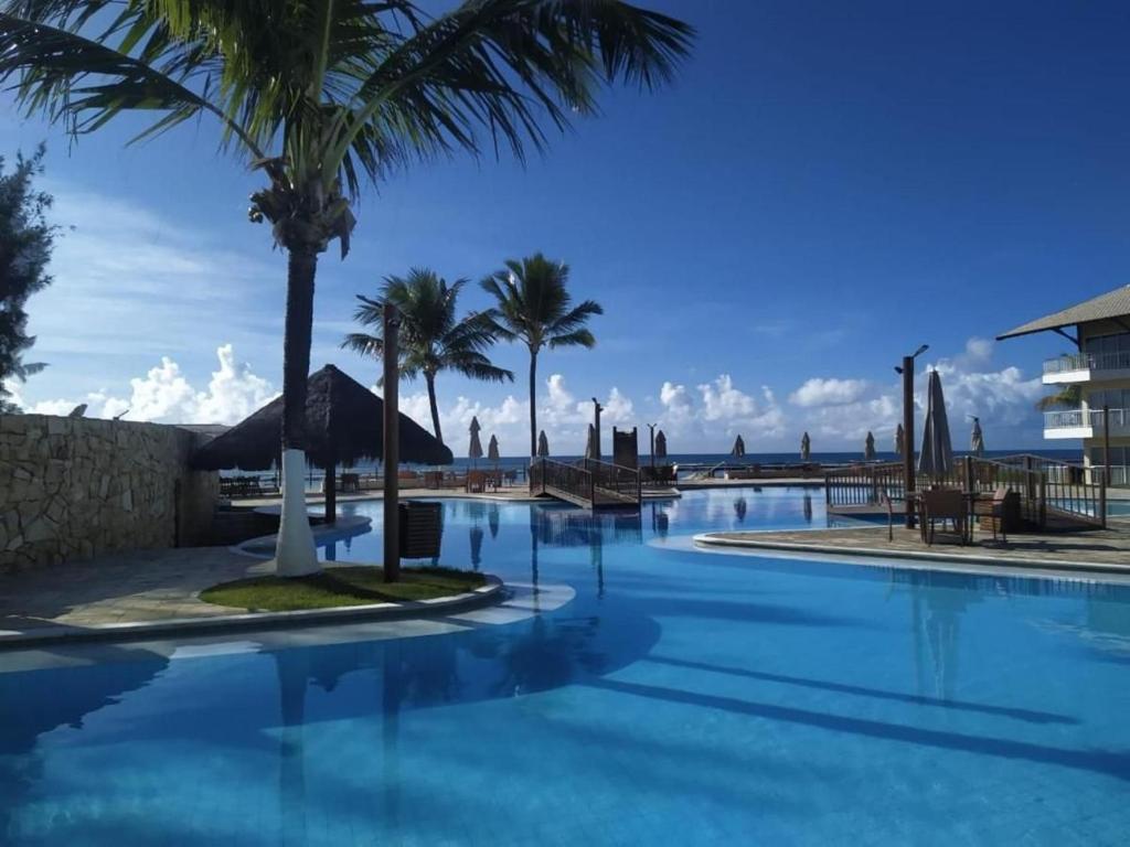 a swimming pool with palm trees in a resort at Muro Alto Marupiara Suítes in Porto De Galinhas