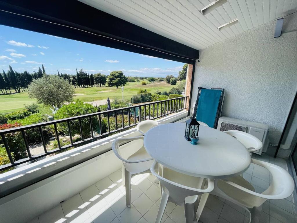 d'un balcon avec une table et des chaises blanches ainsi qu'une grande fenêtre. dans l'établissement Appartement avec piscine, tennis, clim, parking et wifi au Cap d'Agde - FR-1-723-118, au Cap d'Agde