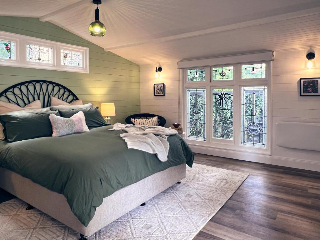 1 dormitorio con 1 cama con sábanas verdes y ventanas en Bundanoon Garden Retreat, en Bundanoon