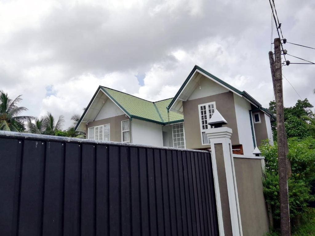 uma casa atrás de uma cerca com um telhado verde em Five Bed two-storey luxury House in 44 perch land in Bandaragama, Sri Lanka em Bandaragama