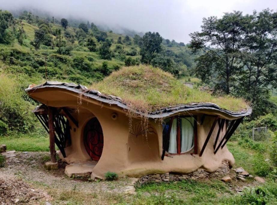 una pequeña casa con techo de hierba en una colina en Unique Mud Home With Scenic Mountain Views en Nainital