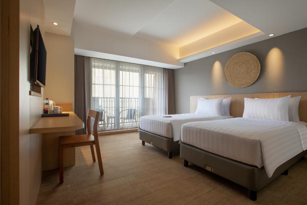 a hotel room with two beds and a desk and a window at Aveta Hotel Malioboro in Yogyakarta