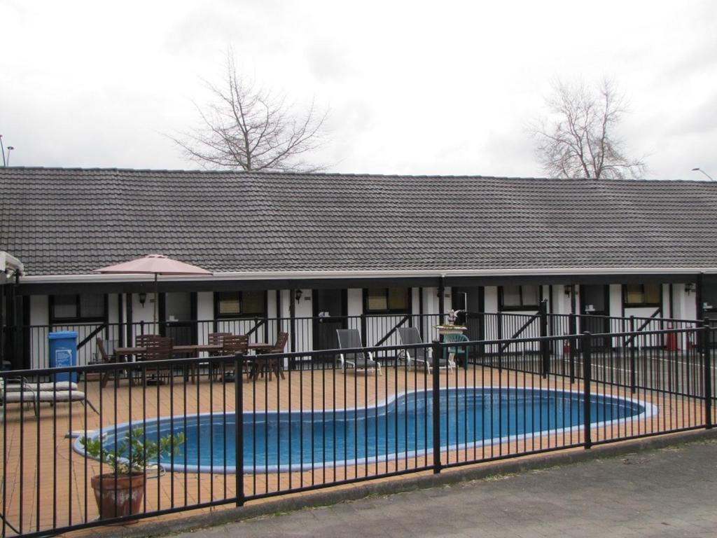 a building with a swimming pool behind a fence at Devonwood Motel in Rotorua
