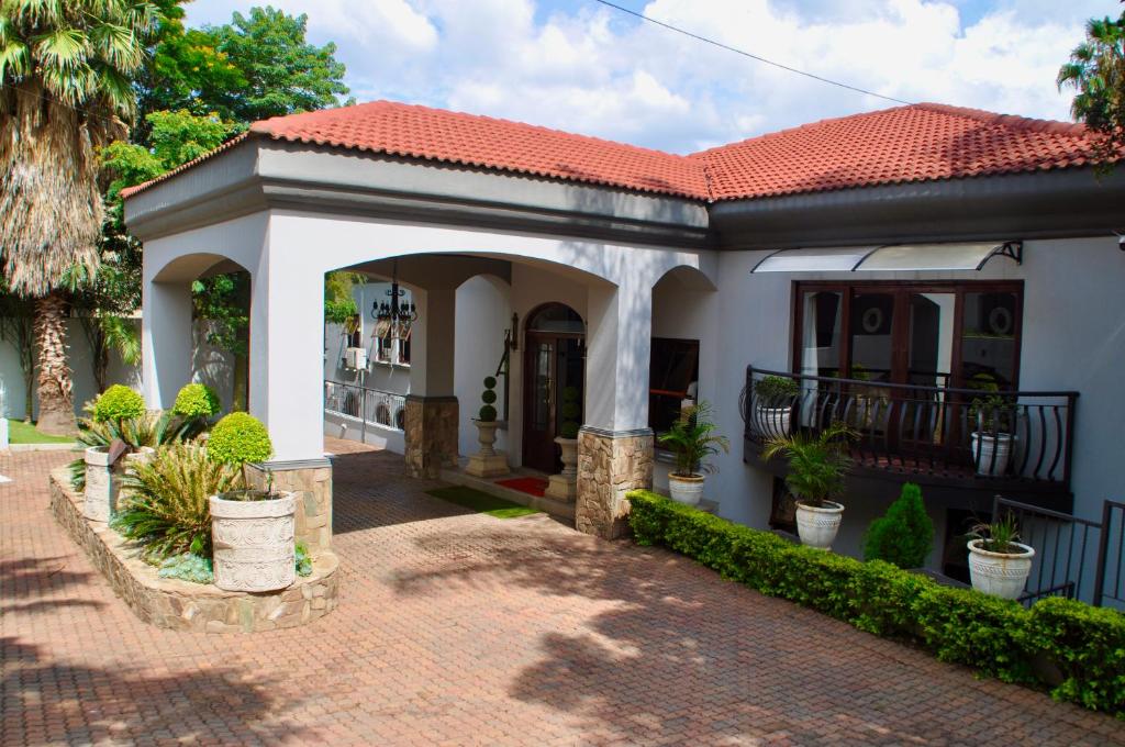 ein kleines weißes Haus mit einer Veranda mit Topfpflanzen in der Unterkunft Ambonnay Terrace Guest House in Pretoria