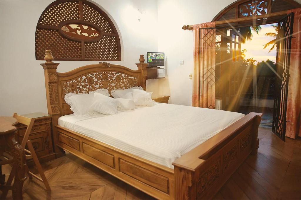 a bedroom with a large wooden bed with white sheets at Preethi Village in Negombo