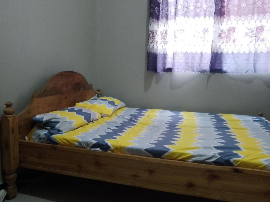 a bed with a blue and yellow comforter and a window at Misyie's HomeStay in Sao Hill