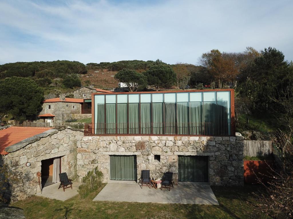 une maison en pierre avec des fenêtres en verre sur une colline dans l'établissement Gerês - Leiras do Tempo - Cottage Tomadinha 2, à Terras de Bouro