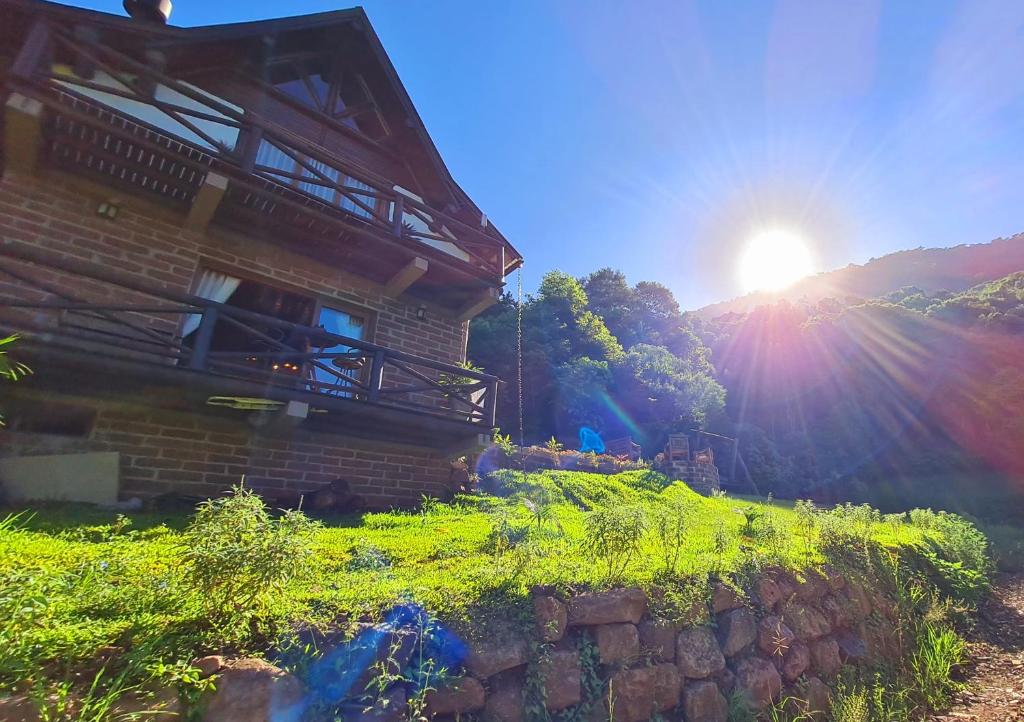 a house on a hill with the sun behind it at Cabana valle Pietra Hospedagem sofisticada em Nova Petrópolis in Nova Petrópolis