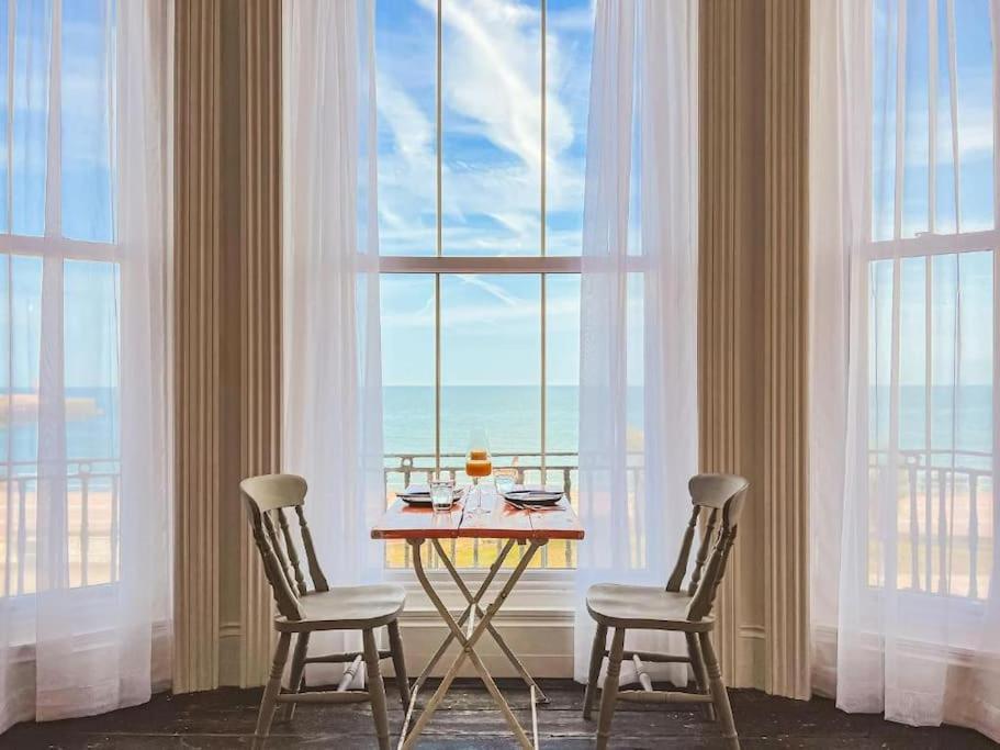 uma mesa e duas cadeiras num quarto com janelas em Beach Apartment em Hastings