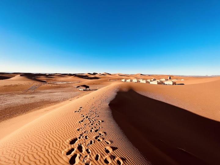a desert with a group of footprints in the sand at Desert Waves Excursion in Mhamid