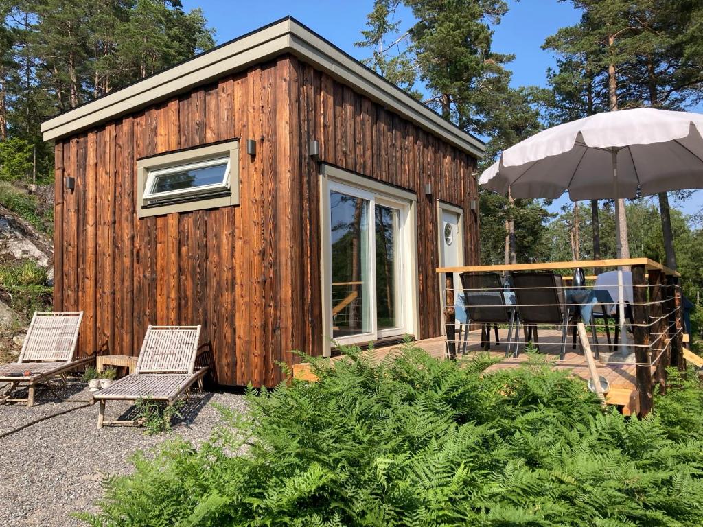 a wooden cabin with two chairs and an umbrella at Fullt utrustat Minihus på landet in Västerhaninge