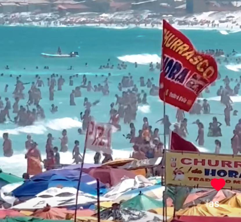 a beach with people in the water and flags at Suite canto do forte in Cabo Frio