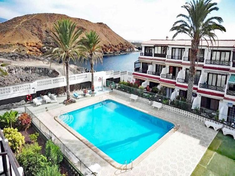 a swimming pool in front of a building with palm trees at Sasha Tenerife in Costa Del Silencio