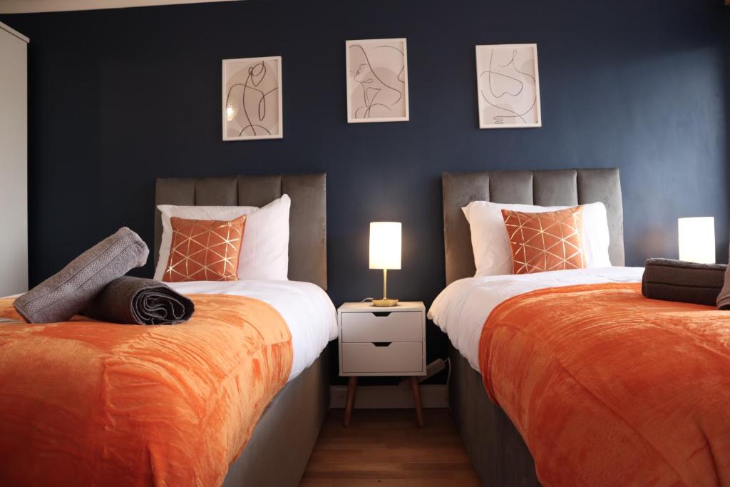 a bedroom with two beds with orange sheets and two lamps at Perfect 2 Bedroom Flat Heathrow, Free Parking in Shepperton