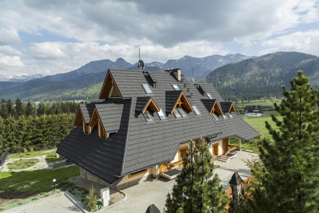 a house with a black roof with mountains in the background at Domy Mountain Premium in Kościelisko