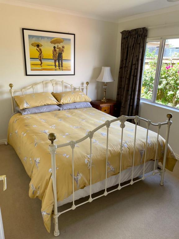 a bedroom with a white bed with yellow sheets and a window at Spacious Home in Paraparaumu