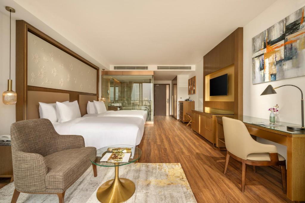 A hotel bedroom with two beds, a compact desk and a separate lounge chair.