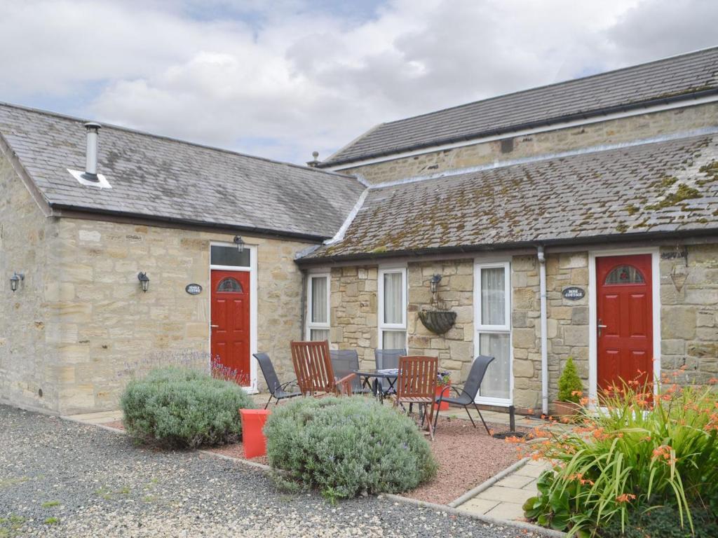 a stone house with red doors and a patio at Rose Cottage - Uk3283 in Guyzance