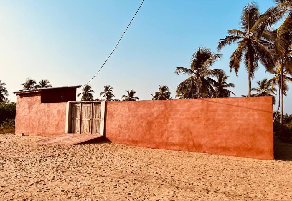 an orange wall with a gate on a beach with palm trees at Amistad in Ouidah