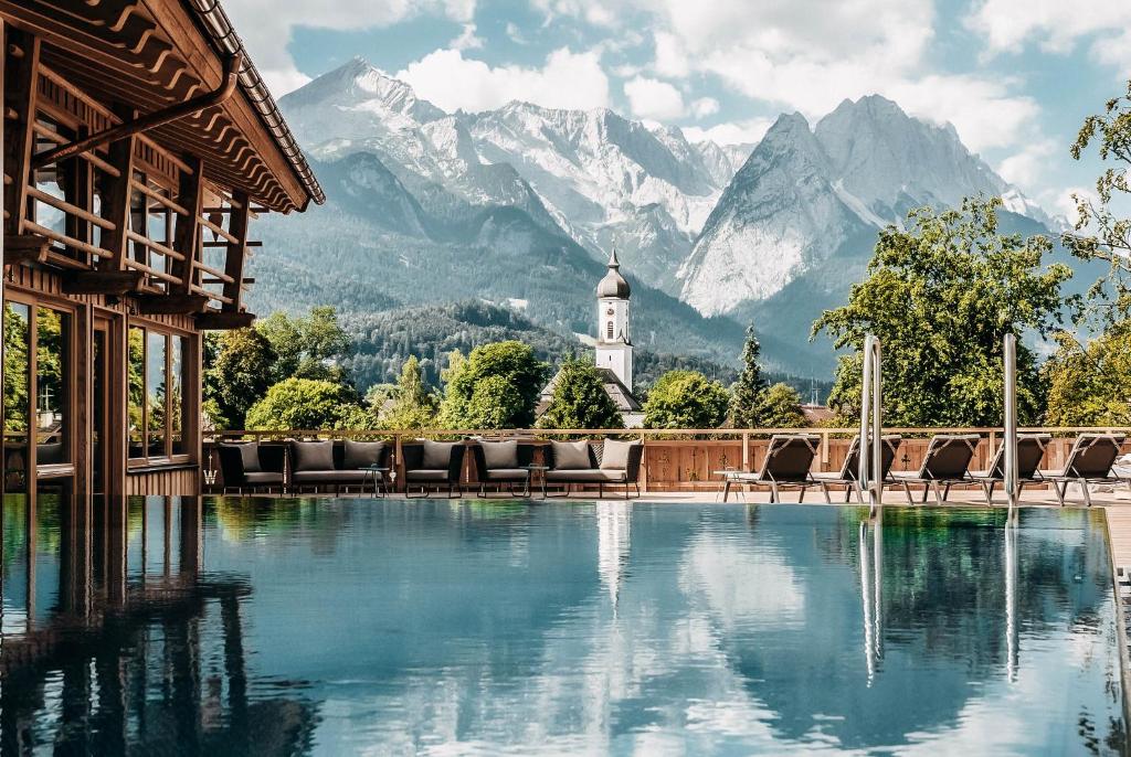 una piscina con sillas y montañas en el fondo en Werdenfelserei en Garmisch-Partenkirchen