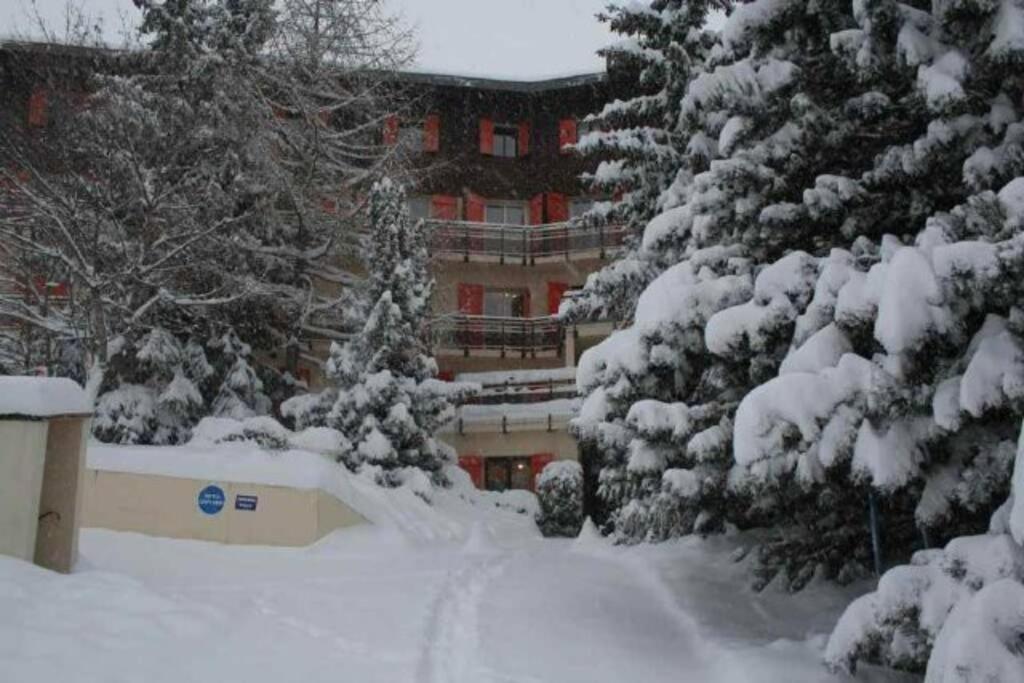 une rue enneigée avec des arbres et un bâtiment dans l'établissement Superbe appartement vue montagne, à Saint-Étienne-de-Tinée