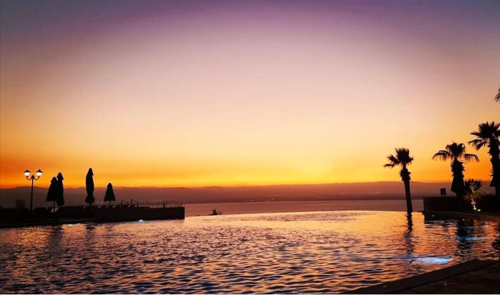 E25 Samarah Resort Apartments في السويمة: مسبح بالنخيل وغروب الشمس في الخلفية