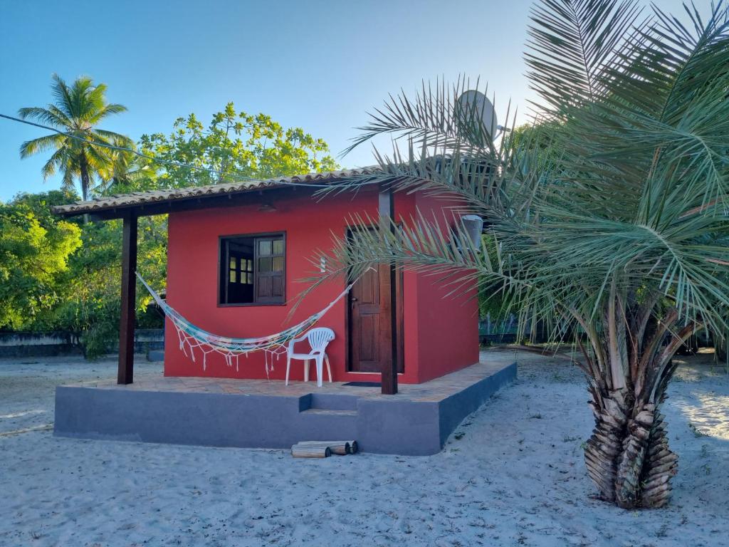 a red house with a hammock next to a palm tree at Chalés Rio Bonito in Imbassai