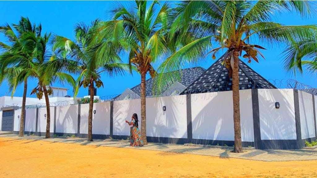 a woman standing next to a white wall with palm trees at Dapi Home Residence in Lomé