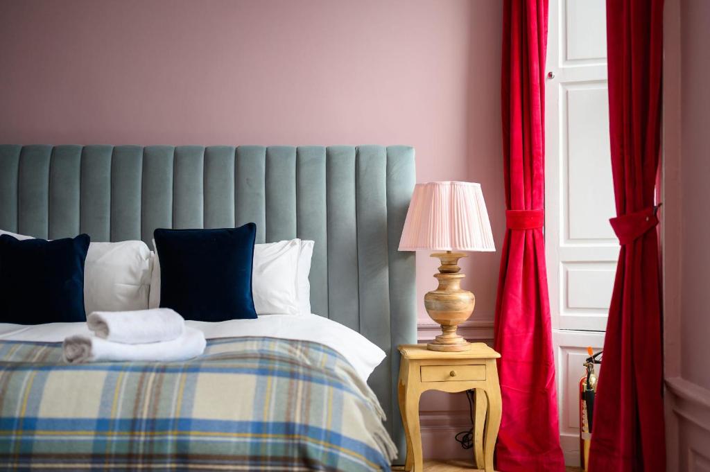 a bedroom with a bed and a lamp and red curtains at Queen Charlotte Guesthouse in Edinburgh