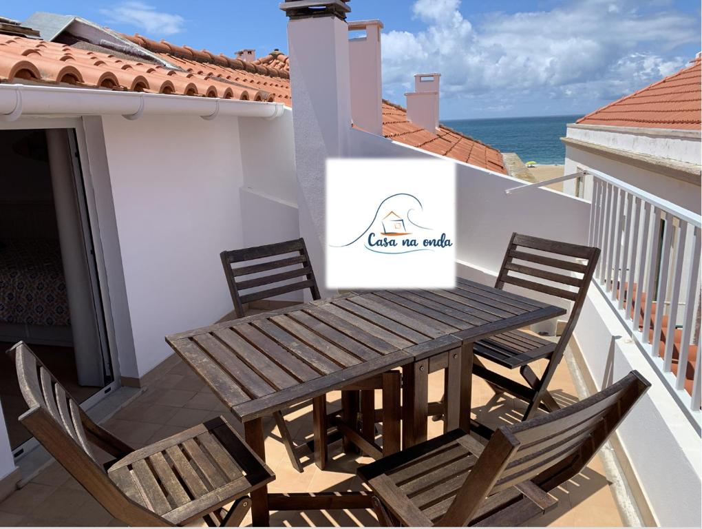 een houten tafel en stoelen op een balkon met uitzicht op de oceaan bij Casa na onda Liberdade in Nazaré