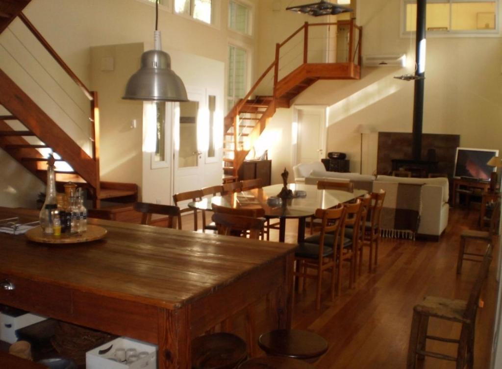 una habitación con mesas y sillas de madera y una escalera en La casa de 10GO en Cariló