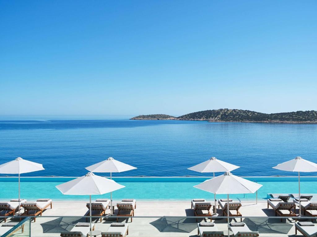 einen Strand mit Liegestühlen und Sonnenschirmen und dem Meer in der Unterkunft NIKO Seaside Resort MGallery in Agios Nikolaos