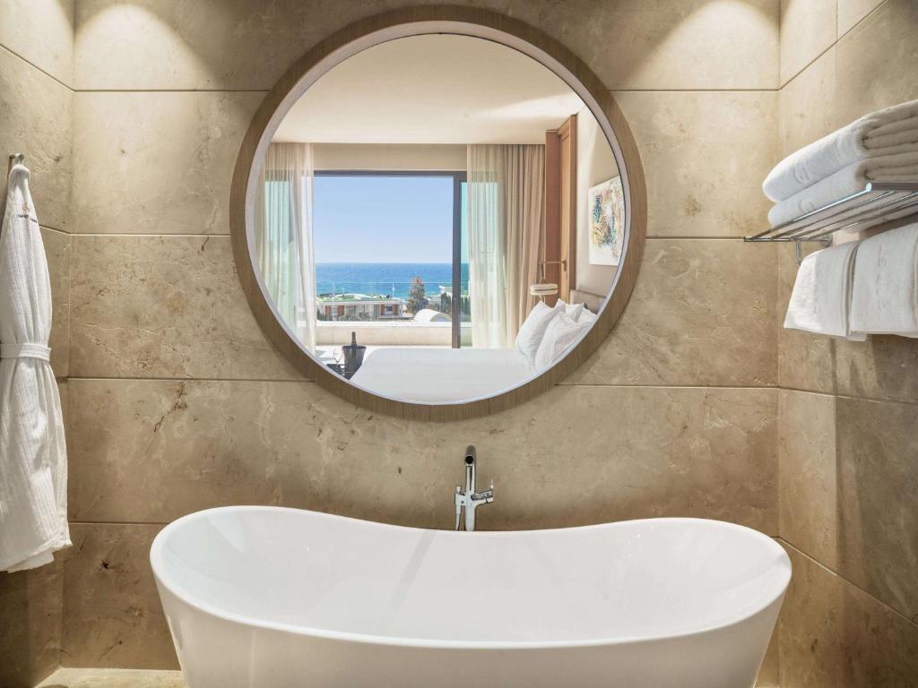 a bathroom with a white tub and a mirror at Cap St Georges Hotel & Resort in Peyia