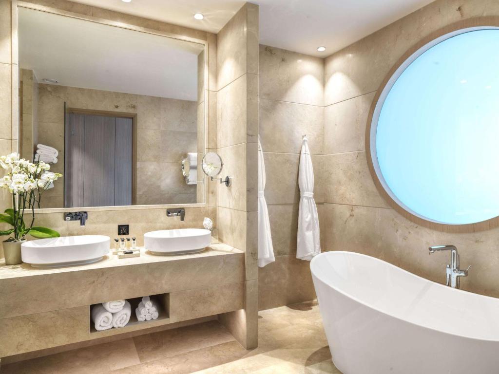 a bathroom with two sinks and a tub and a mirror at Cap St Georges Hotel & Resort in Peyia