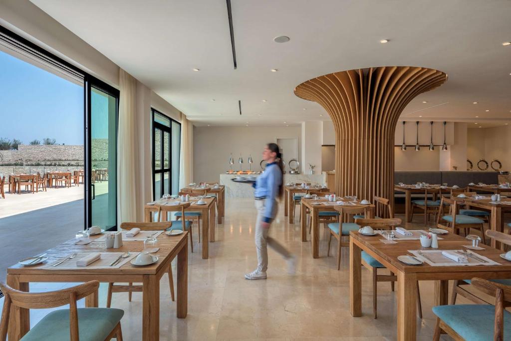 a woman walking through a dining room with tables at Cap St Georges Hotel & Resort in Peyia