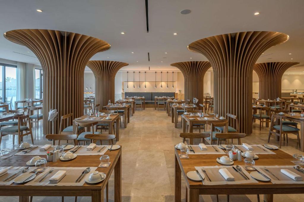 a restaurant with wooden tables and chairs and windows at Cap St Georges Hotel & Resort in Peyia