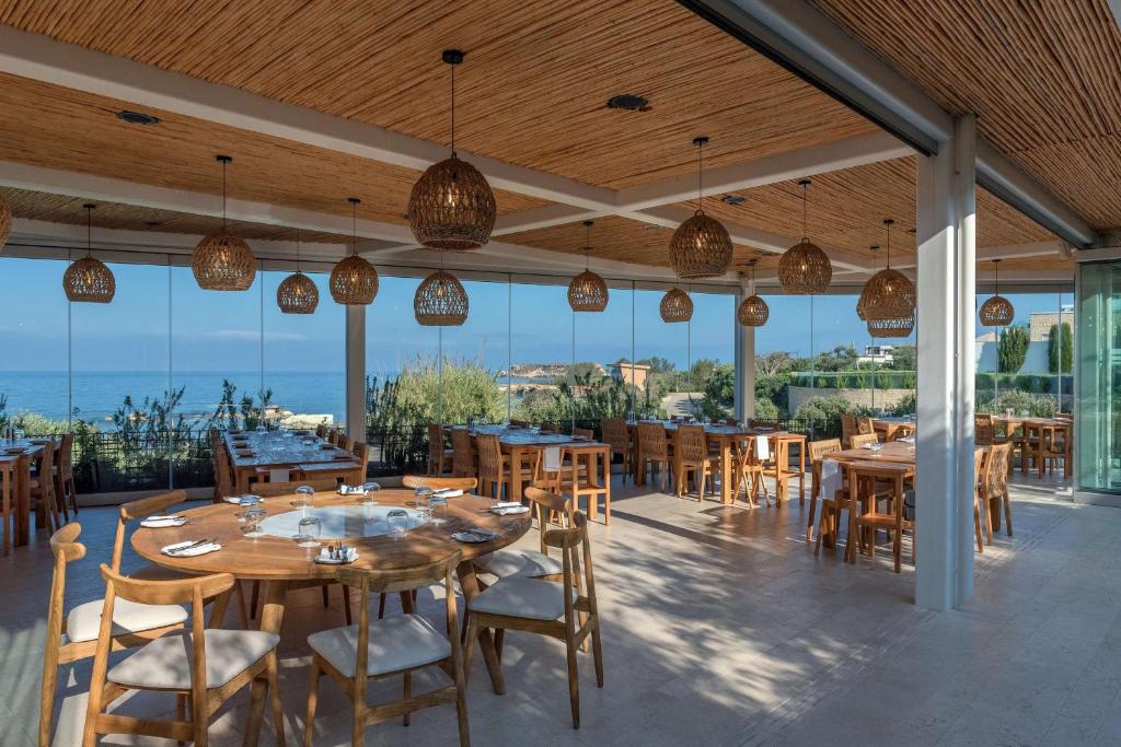 a restaurant with wooden tables and chairs and windows at Cap St Georges Hotel & Resort in Peyia