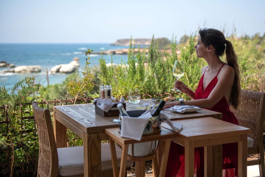 a woman sitting at a table with a glass of wine at Cap St Georges Hotel & Resort in Peyia
