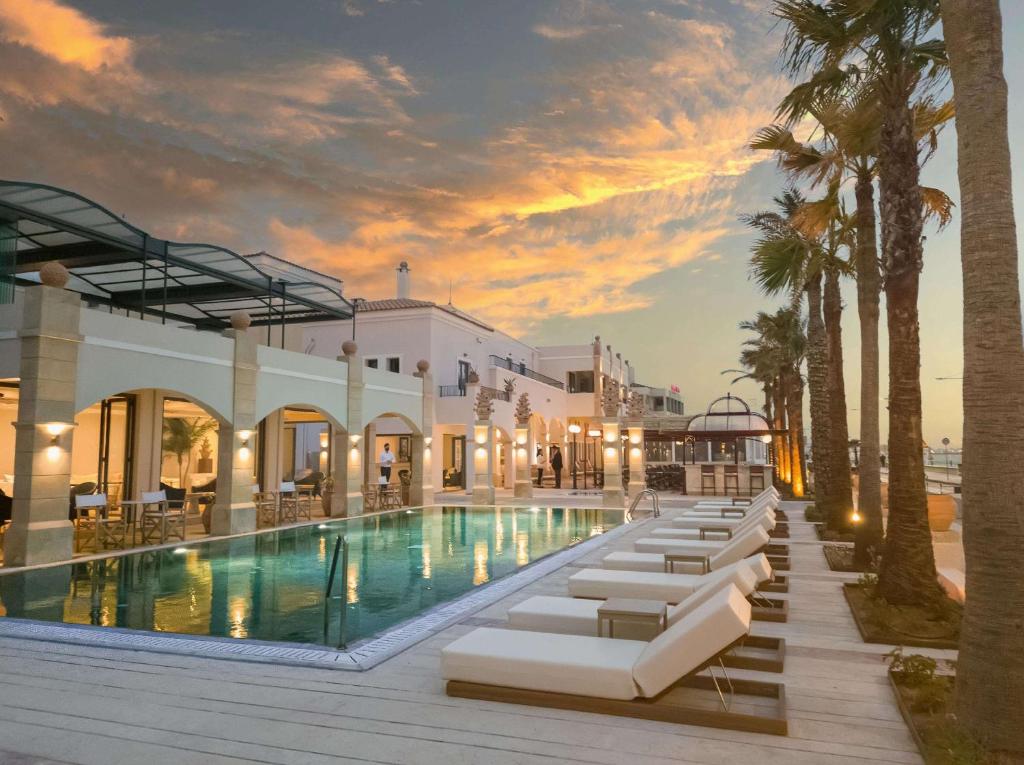 a resort pool with lounge chairs and palm trees at Grecotel Plaza Beach House in Rethymno Town