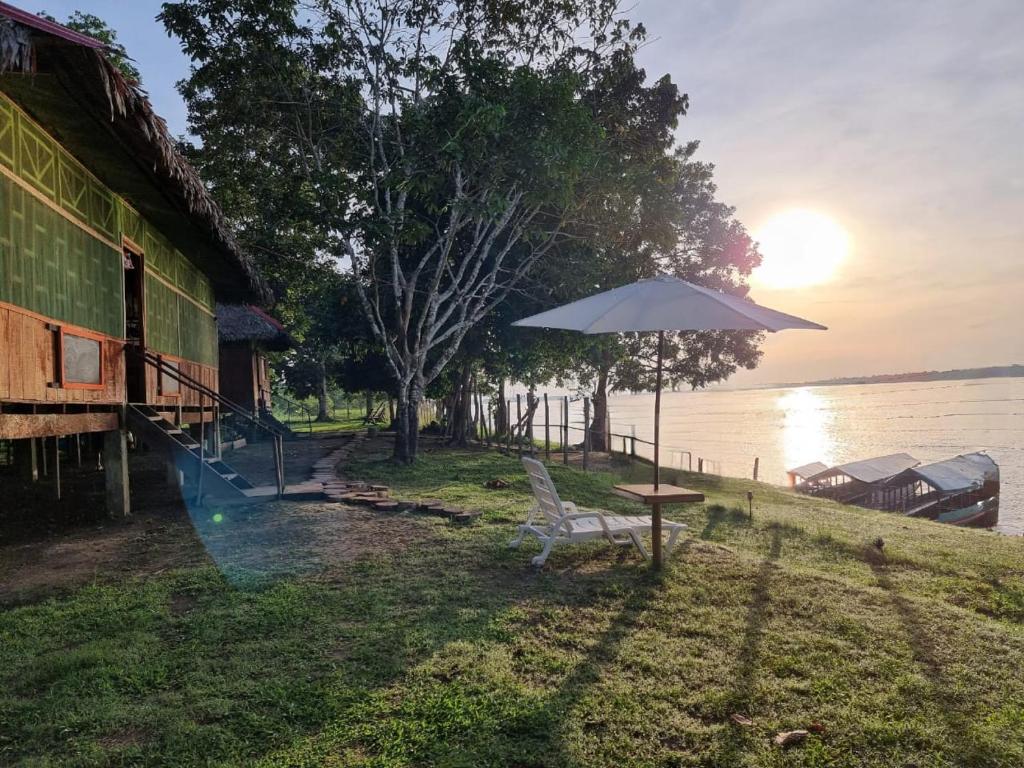einen Tisch und einen Stuhl mit einem Regenschirm neben dem Wasser in der Unterkunft Milía Amazon Lodge in Iquitos