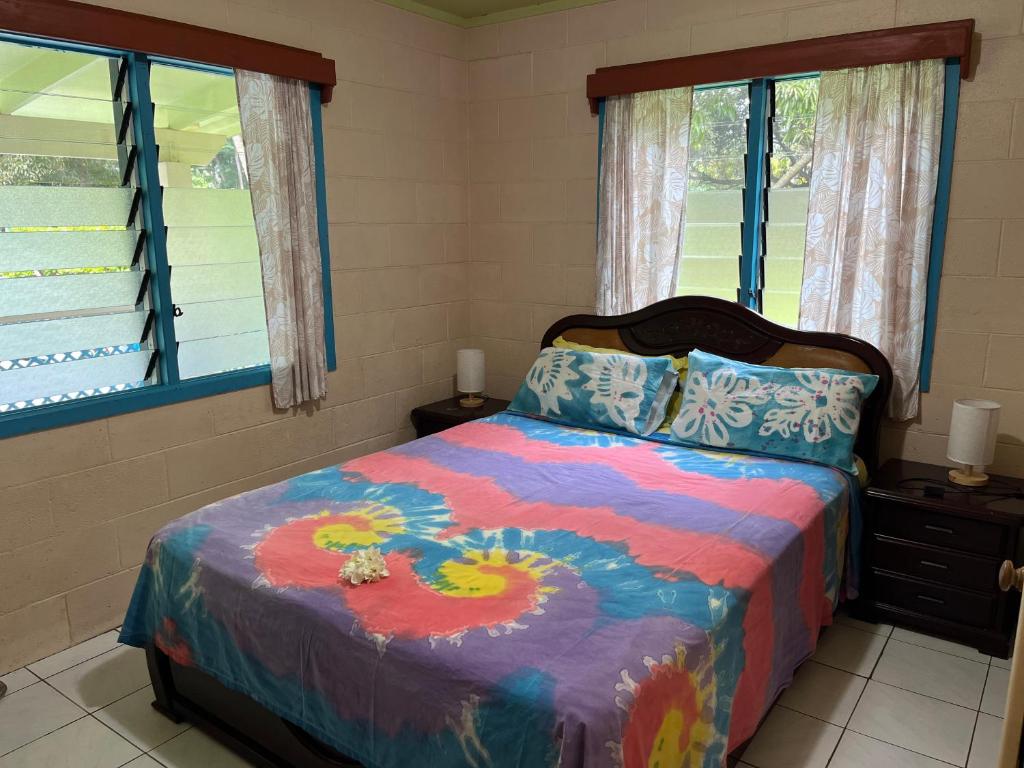 1 Schlafzimmer mit einem farbenfrohen Bett und 2 Fenstern in der Unterkunft Sharnyta’s Guesthouse in Avarua