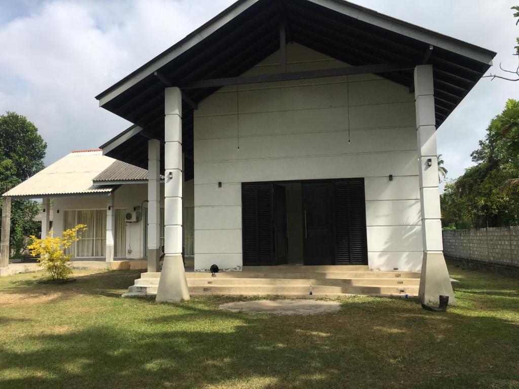 a white house with a black roof and a dog on the porch at Coconut House in Panadura