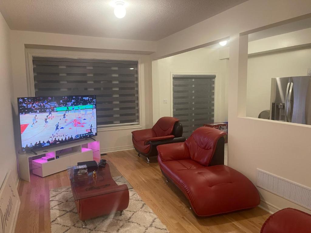 a living room with a flat screen tv and red chairs at Comfort King in Oshawa