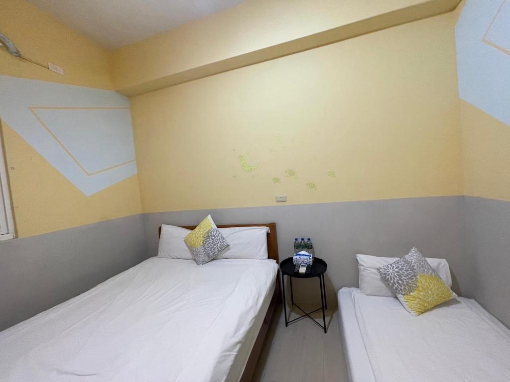 two twin beds in a room with a side table at 萩閣民宿Sara&#39;s House走路可到夜市近市區好停車 in Hualien City