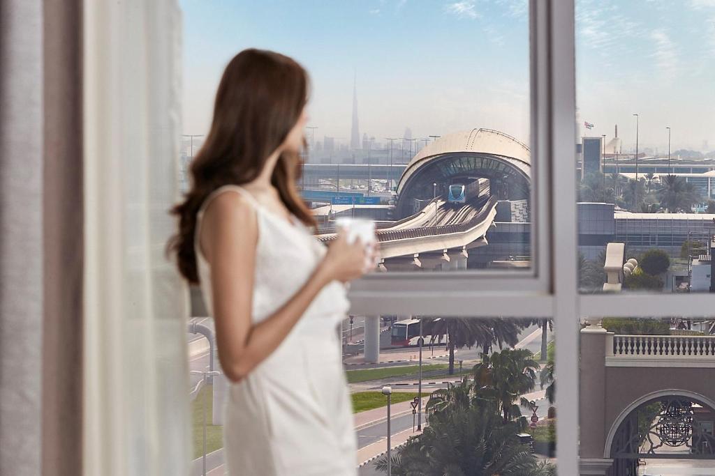 a woman in a white dress looking out of a window at Flora Al Barsha Hotel At The Mall in Dubai