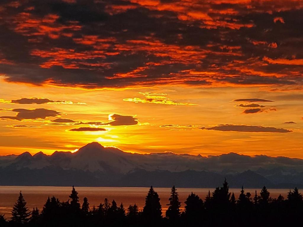 a sunset over the mountains and water with trees at Bluff Hideaway - Guest House in Homer