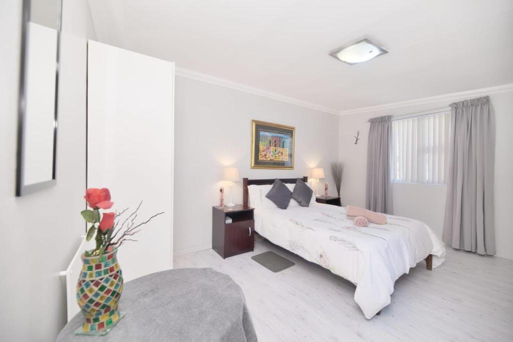 a white bedroom with a bed and a vase of flowers at Redsky self catering Agulhas in Agulhas