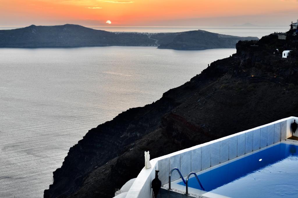 a person standing on the side of a cliff next to the ocean at Aeolos Art & Eco Suites Adults Only in Imerovigli