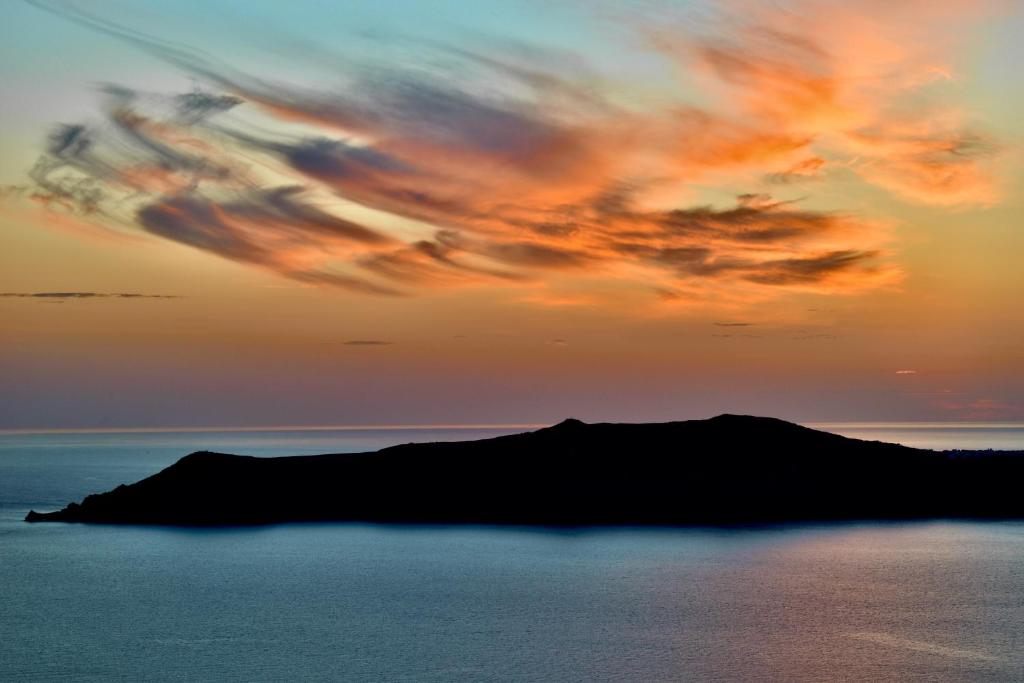 a sunset over a small island in the ocean at Aeolos Art & Eco Suites Adults Only in Imerovigli
